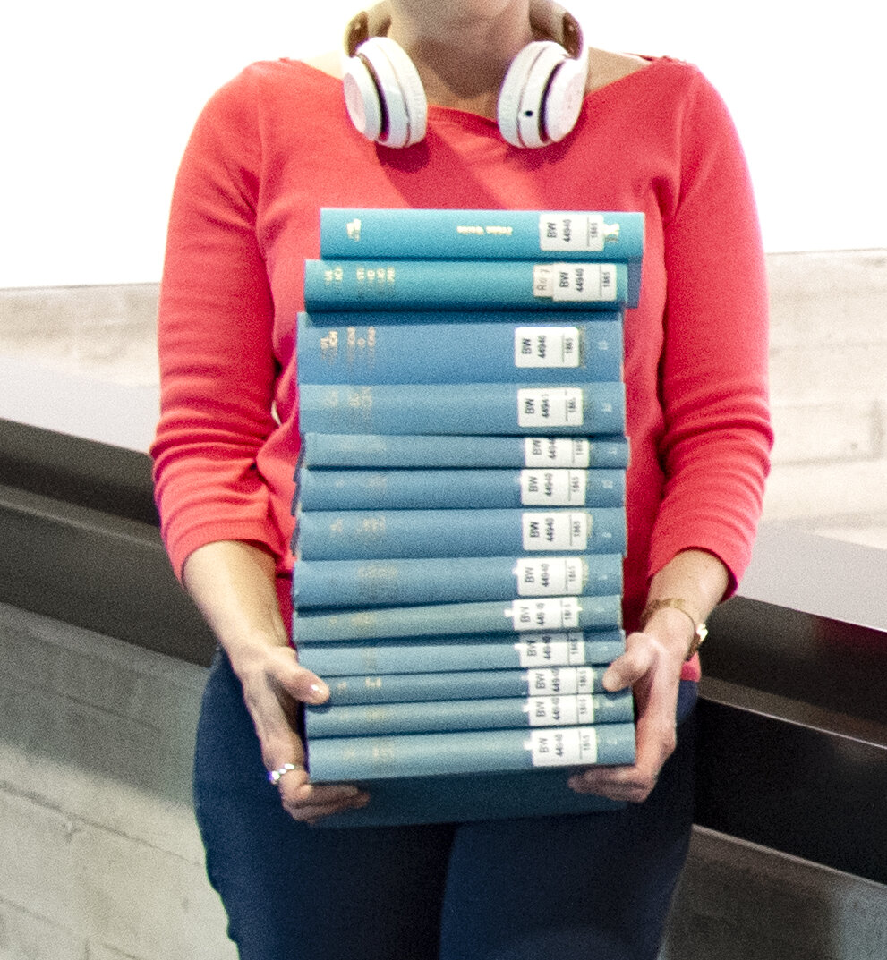 Ausleihen © GWLB/Wollenberg Eine Frau trägt einen großen Stapel Bücher.