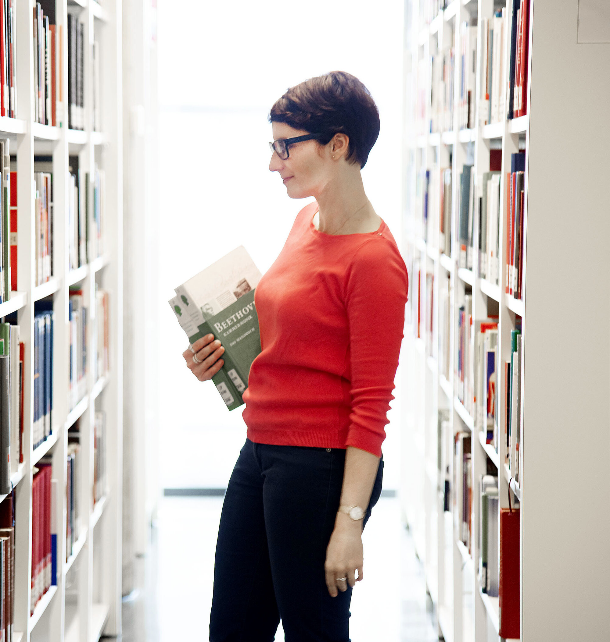 Ausleihen © GWLB/Wollenberg Ein Frau steht suchend zwischen zwei Bücherregalen.
